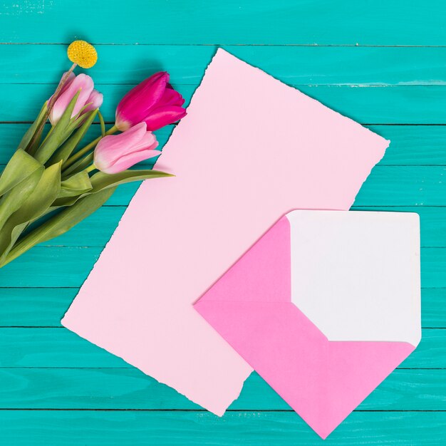 High angle view of blank paper; open envelop and tulip flowers over wooden backdrop