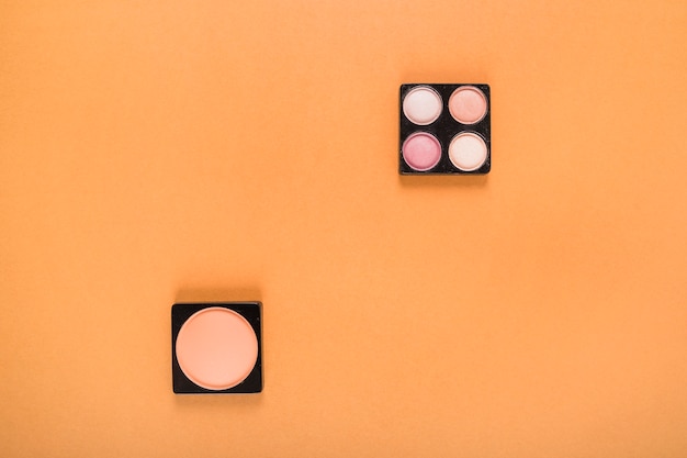 High angle view of blusher and eye shadow powders on orange background