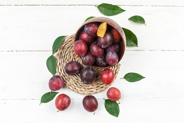 Free photo high angle view a bowl of plums on wicker placemat on white wooden board surface. horizontal