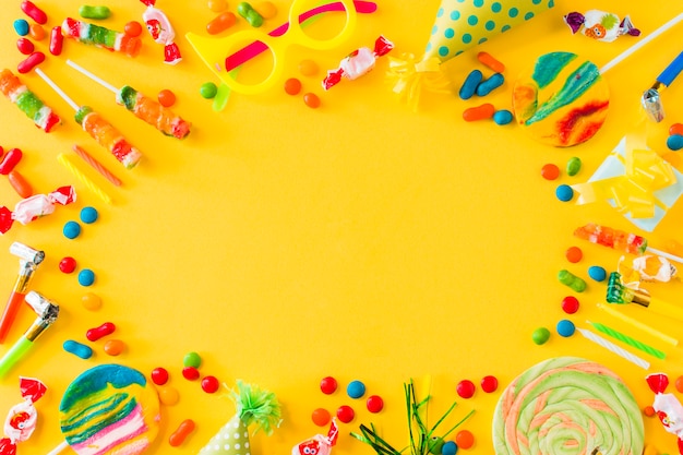 High angle view of candies; lollipops; candles; party at and blower on yellow surface