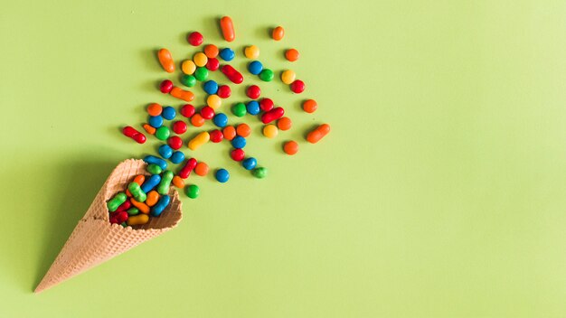High angle view of candies spilling from waffle ice cream cone on green background