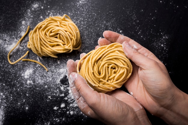 Взгляд высокого угла шеф-повара держа гнездо макаронных изделий спагетти над рабочей поверхностью кухни