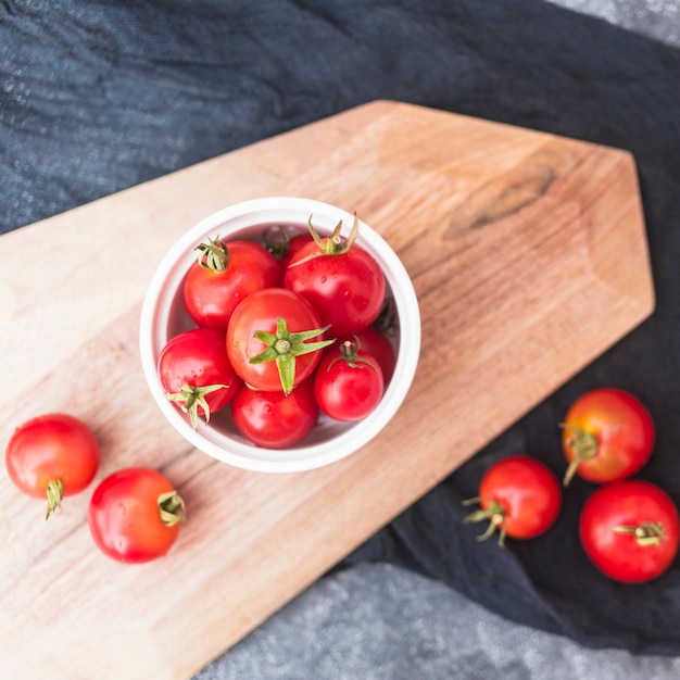 High angle view of cherry tomatoes in container on wooden chopping board