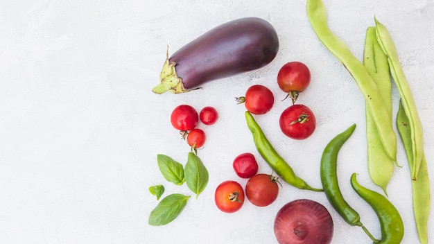 High angle view of cherry tomatoes; hyacinth beans; basil; onion and green chili peppers on white backdrop