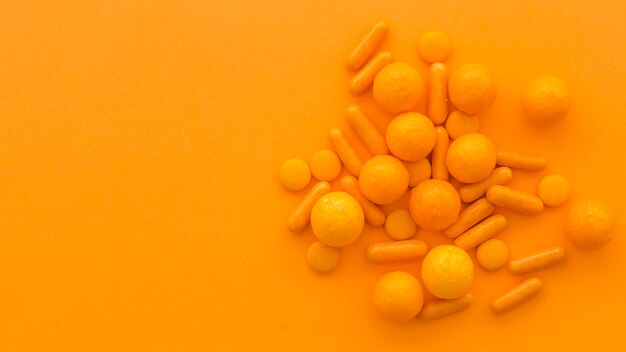 High angle view of circular and capsule shape candies on orange background