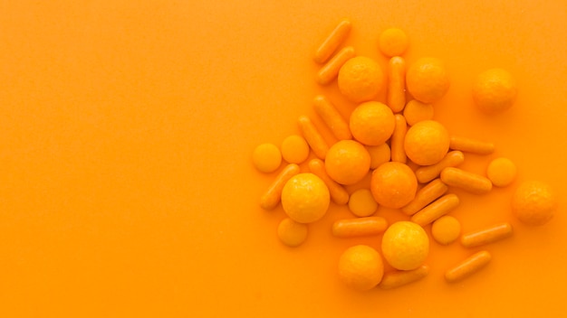High angle view of circular and capsule shape candies on orange background