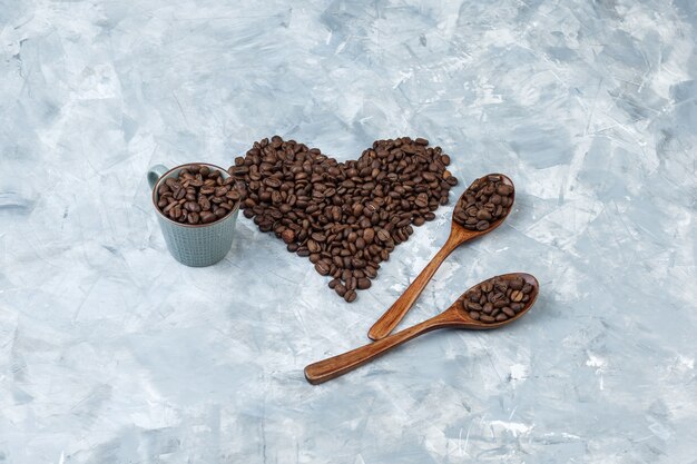 灰色の漆喰の背景にカップと木のスプーンで高角度ビューのコーヒー豆。水平