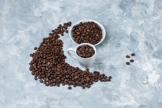 High angle view coffee beans in white cup and plate on grey plaster background. horizontal