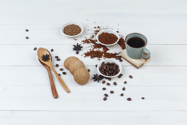 High angle view coffee in cup with coffee beans, grinded coffee, spices, cookies, wooden spoons on wooden background. horizontal