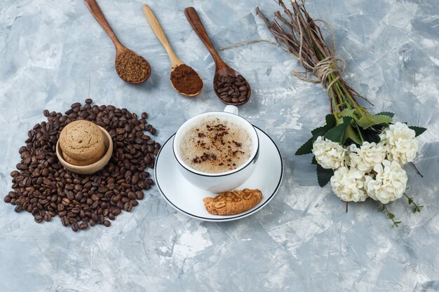 High angle view coffee in cup with cookies, coffee beans, grinded coffee, flowers on grungy grey background. horizontal