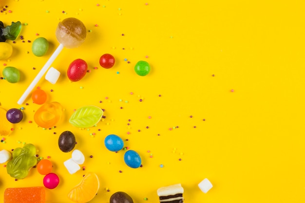 High angle view of colorful candies and lollipops on yellow backdrop