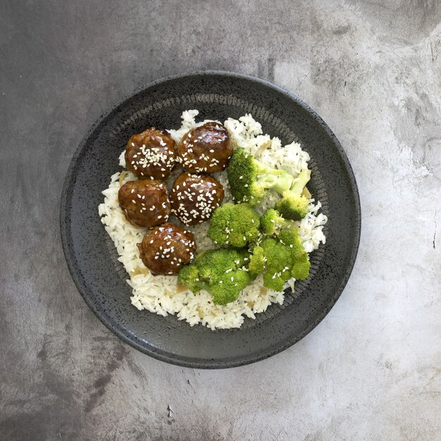 High angle view of cooked rice with meatballs and broccoli in a plate on the table