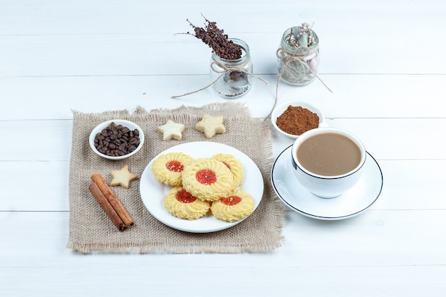 High angle view cookies, cinnamon, coffee beans on piece of sack with cup of coffee, bowl of instant coffee, ropes on white wooden board background. horizontal