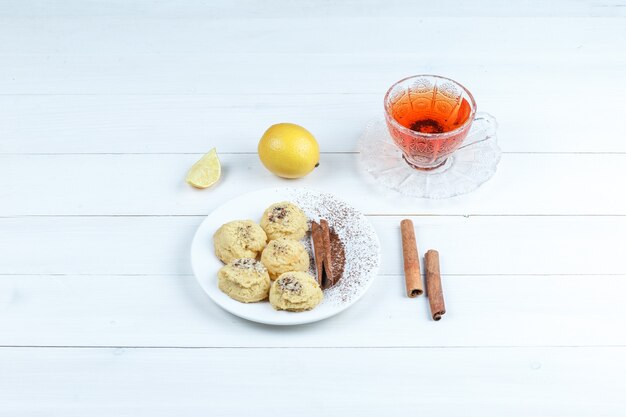 High angle view cookies, cup of tea with cinnamon, lemon on white wooden board background. horizontal