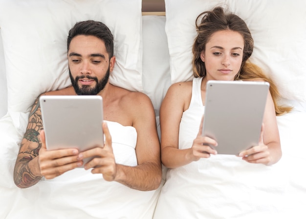 High angle view of couple using digital tablet on bed