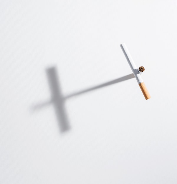 Free photo high angle view cross sign made from cigarette with it shadow on isolated on white background