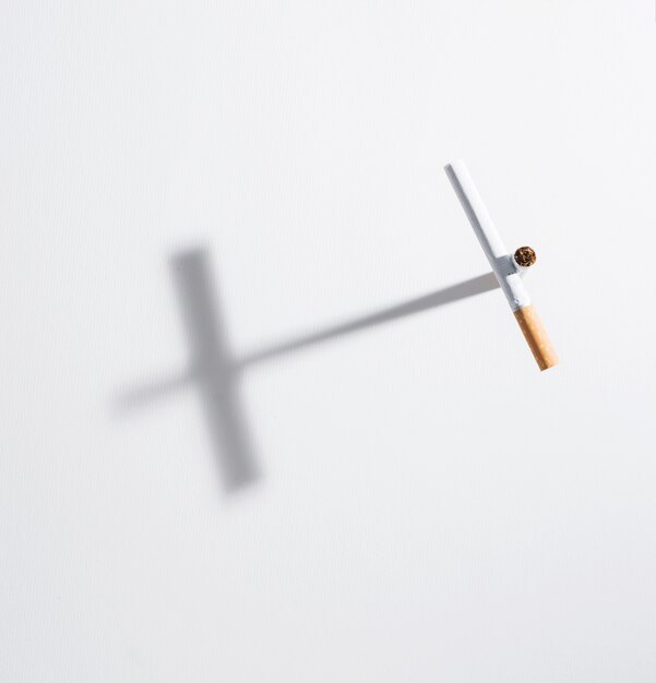 High angle view cross sign made from cigarette with it shadow on isolated on white background