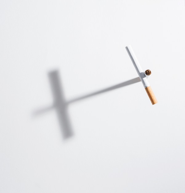 Высокий угол обзора крест знак из сигареты с ним тень на белом фоне