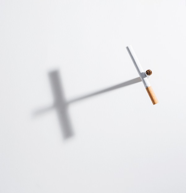Высокий угол обзора крест знак из сигареты с ним тень на белом фоне