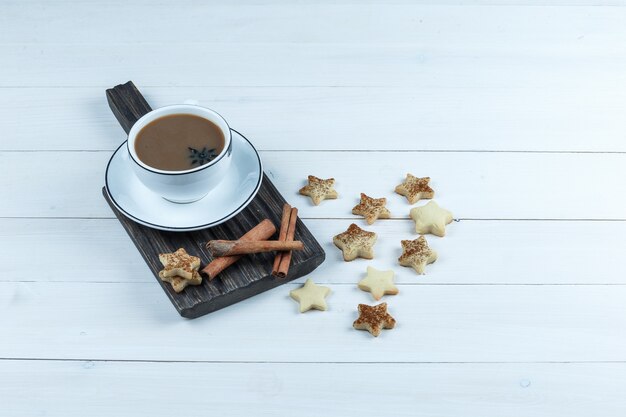 High angle view cup of coffee, cinnamon on cutting board with star cookies on white wooden board background. horizontal