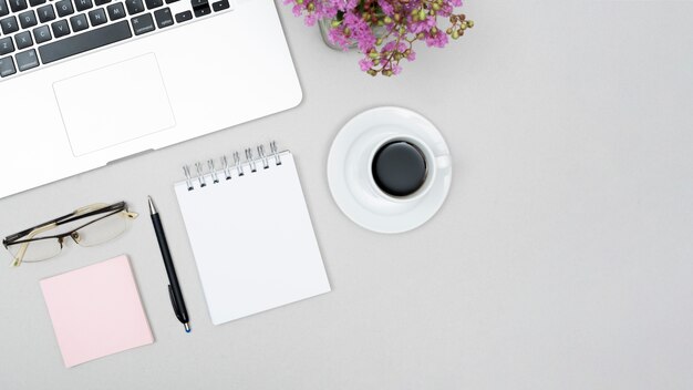 Высокий угол обзора чашки кофе; ноутбук; очковое; спиральный блокнот цветочный горшок на сером столе