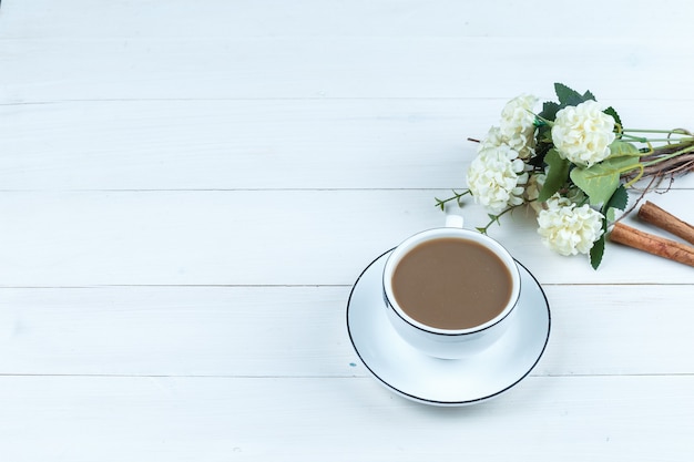 High angle view cup of coffee with flowers, cinnamon on white wooden board background. horizontal