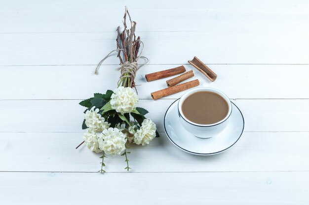 High angle view cup of coffee with flowers, cinnamon on white wooden board background. horizontal