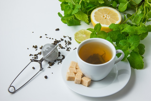 Взгляд высокого угла чашка чаю с лимоном, сахаром, листьями мяты на белой поверхности. горизонтальный