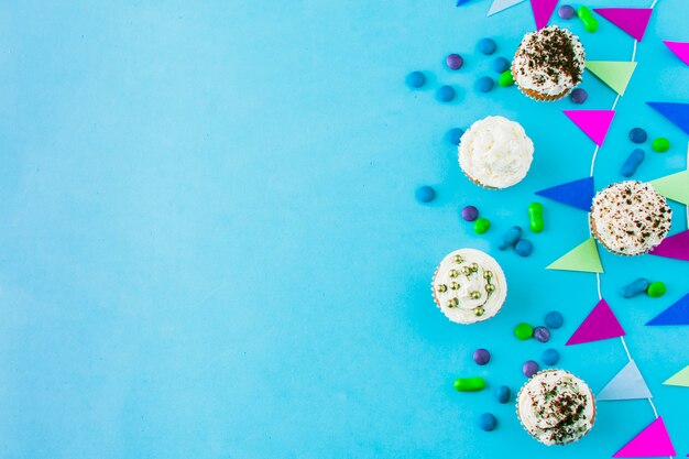 High angle view of cupcakes; candies and bunting on blue backdrop