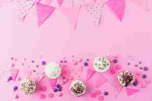 Free photo high angle view of cupcakes; candies and bunting on pink background