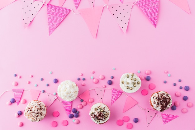 High angle view of cupcakes; candies and bunting on pink background