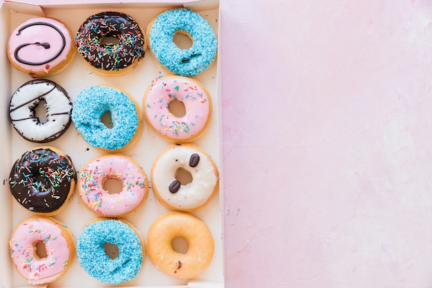 High angle view of delicious donuts in box on pink surface