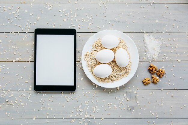 Free photo high angle view of digital tablet near eggs with oats on plate