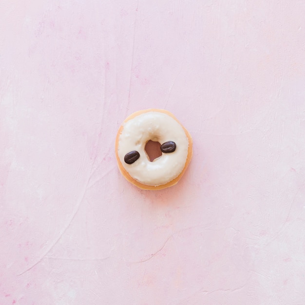 Высокий угол зрения пончик, украшенный кофейными зернами на розовом фоне