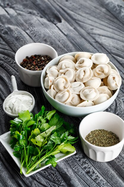 High angle view dough in bowl with greens, spices on gray wooden surface. vertical