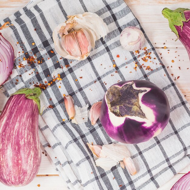 High angle view of eggplants; onion and garlic cloves on chequered pattern cloth