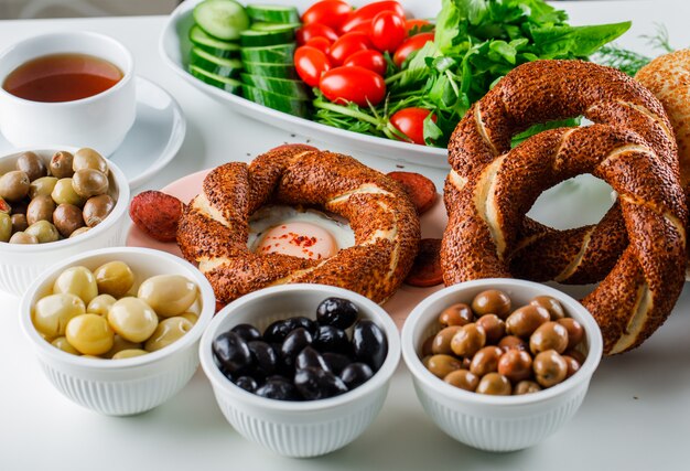 High angle view eggs with sausage in plate with a cup of tea, turkish bagel, salad on white surface