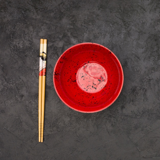 High angle view of empty chinese bowl and wooden chopsticks over textured black background