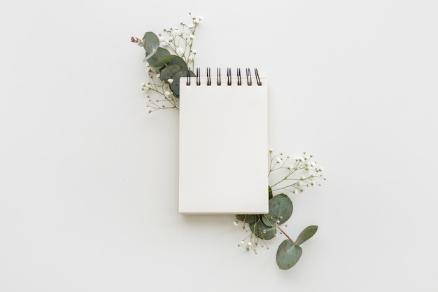High angle view of empty spiral notepad with leafs and baby's breath flowers on white surface