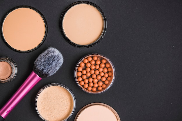High angle view of face powder; bronzing pearls and makeup brush on black backdrop