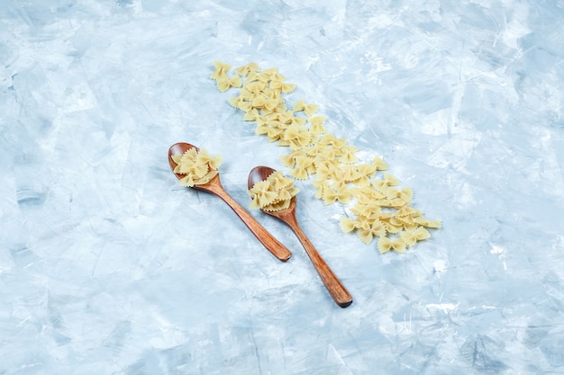 High angle view farfalle pasta in wooden spoons on grungy grey background. horizontal
