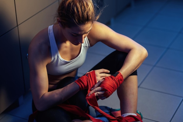 High angle view of female fighter preparing for exercising and wrapping hands with bandages in locker room