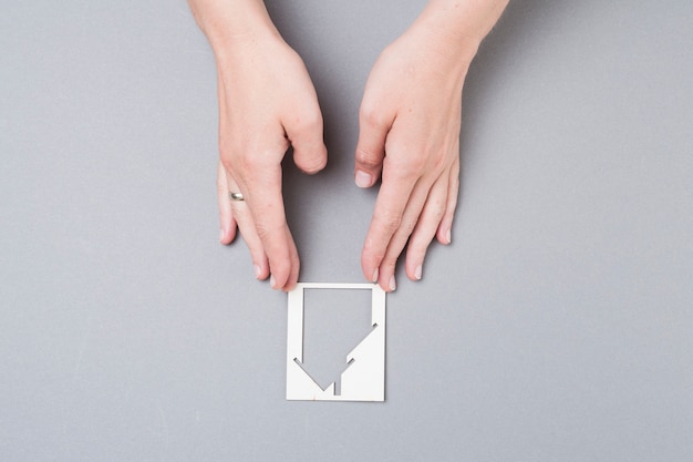 High angle view of female hand touching house cutout on grey background