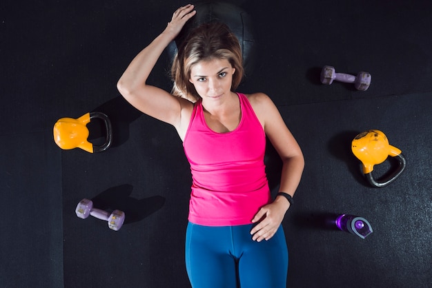 High angle view of fit woman relaxing on floor near exercise equipments