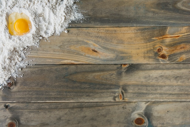 High angle view of flour and egg on wooden background