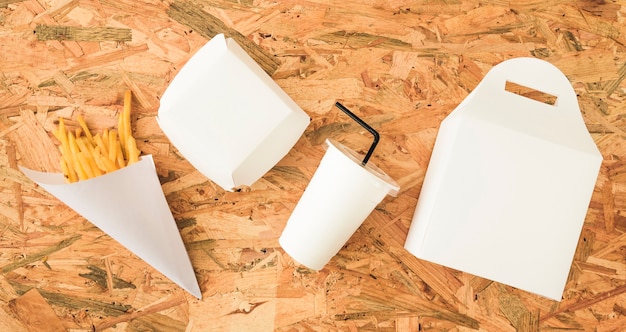 High angle view of french fries; disposal cup and packages on wooden surface