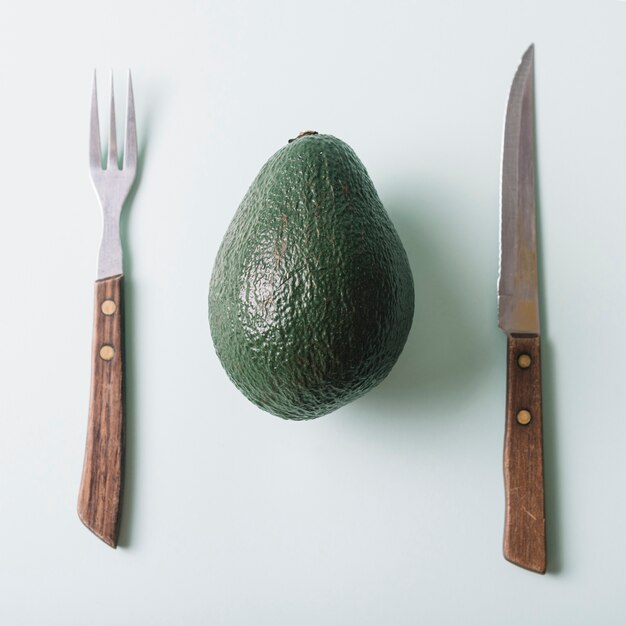 High angle view of fresh avocado; knife and fork on green surface