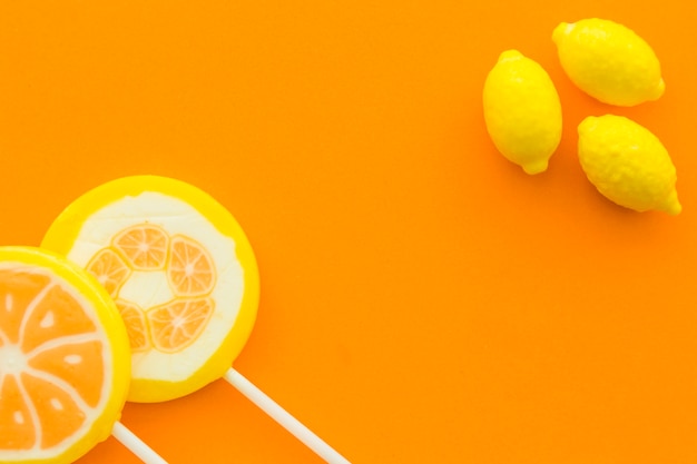 High angle view of fresh citrus fruit lollipops and lemon candies on orange background