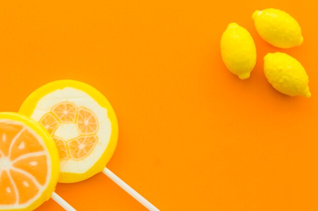 オレンジ色の背景に、新鮮な柑橘類の果物のロリポップとレモンのキャンデーの高い角度のビュー