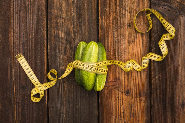 High angle view of fresh cucumbers and measuring tape on wooden background